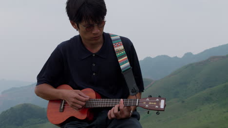 cute asian young artist male playing the ukelele in tropical highlands