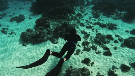 Freediver-in-wetsuit-hover-over-shallow-depth-around-coral-white-sand-seabed,-slow-motion