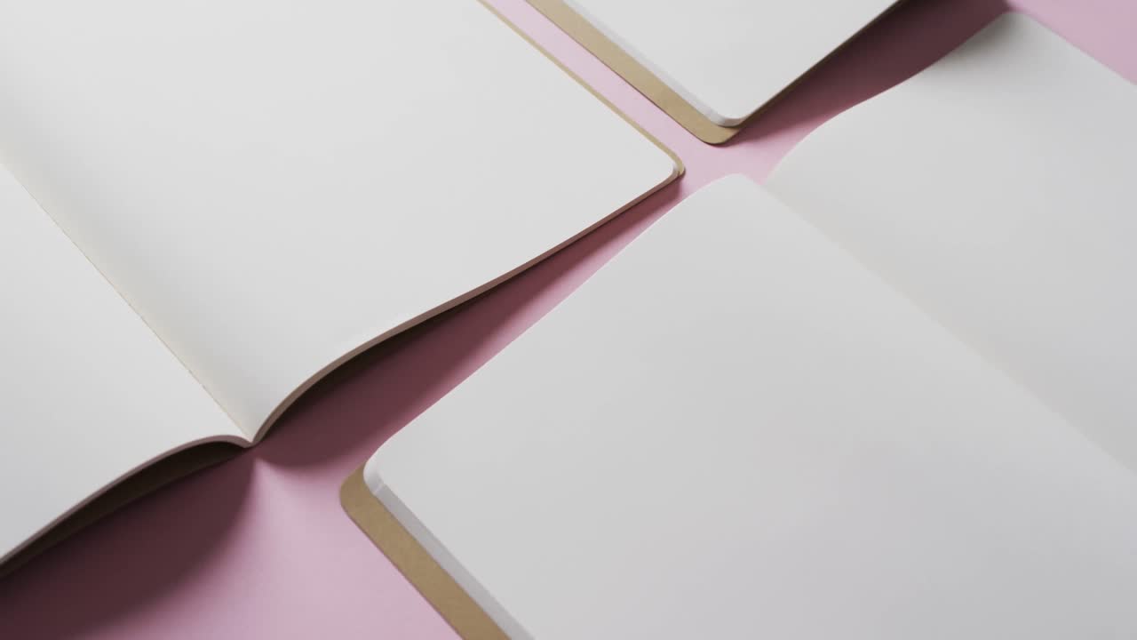Close up of open blank books with copy space on pink background in slow motion