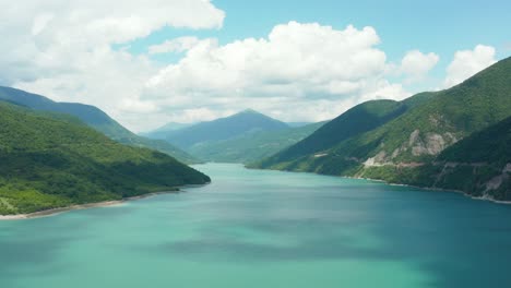 Stunning-aerial-establishing-shot-of-mountain-valley-turquoise-lake-surrounded-by-lush-forest