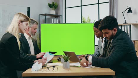 atractivo confiado exitoso experimentado multi-racial hombre y mujer socios de negocios trabajando juntos en la sala de juntas moderna cerca de pantalla de croma verde
