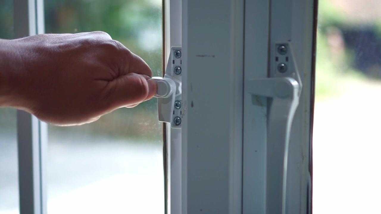Human hand unlocking and opening a white window frame indoors. Home safety, privacy, and everyday household routine concept.