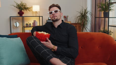 Guy-sitting-on-couch-eating-popcorn-and-watching-interesting-TV-serial,-sport-game-online-at-home