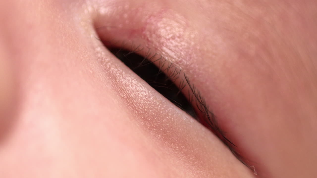 신생아가 부드럽고 편안한 침대 위에서 잠에서 깨어나려고 하는 것처럼 눈을 약간 열고 있다.