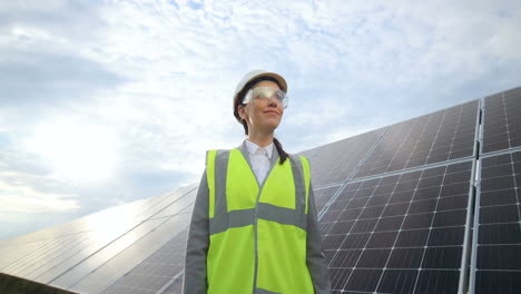 vista inferior de una joven ingeniera caucásica con casco blanco y gafas en un panel solar