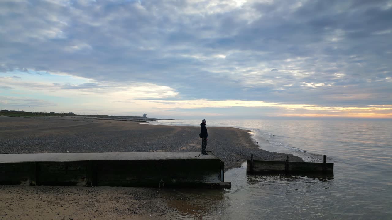 hombre en el muelle mirando hacia el mar al atardecer en la playa de fleetwood, lancashire, reino unido