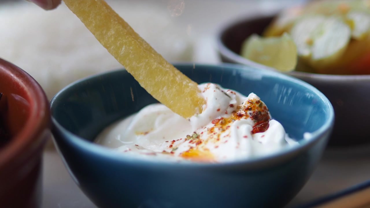 Hand Dipping French Fry into Spiced Yogurt Dip