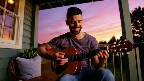 man playing guitar on a porch at sunset