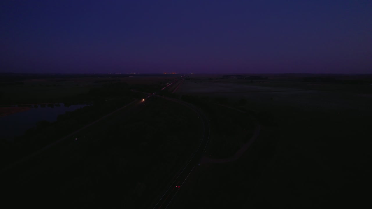 Distant locomotive advances along country tracks at blue hour, headlights cutting a purple horizon over quiet farmland. North Platte, Nebraska, USA