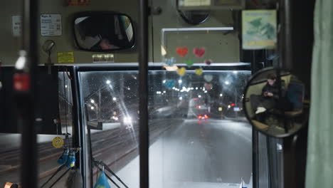 vista interior de un coche conduciendo en una autopista por la noche, mostrando el tablero iluminado, los reflejos del espejo retrovisor y las luces de la ciudad afuera, con otros coches en movimiento