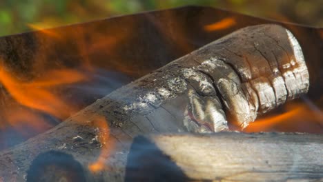 burning wood an coals in rusty portable outdoor bbq grill in sunny day, close up shot