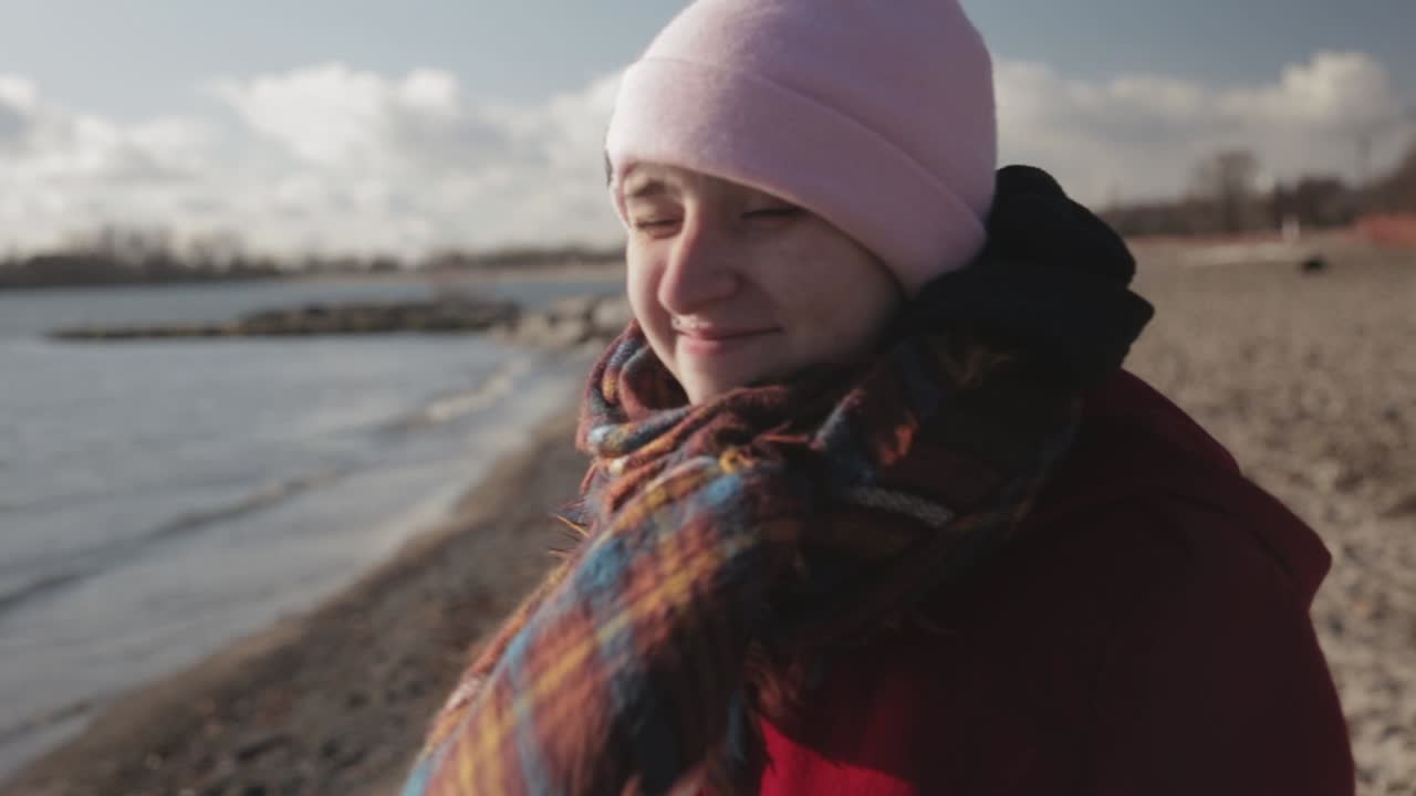joven turista con chaqueta roja, gorro rosa parado en la orilla del lago y disfrutando del día soleado - perfecto para las vacaciones de verano - primer plano
