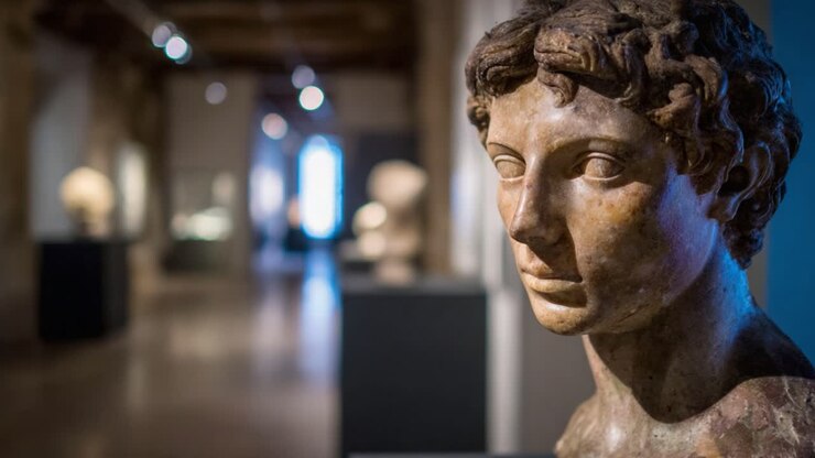 Una scultura antica realizzata meticolosamente che mette in mostra i dettagliati tratti somatici ed espressioni di una figura maschile, catturando l'essenza dell'arte classica in un ambiente espositivo.
