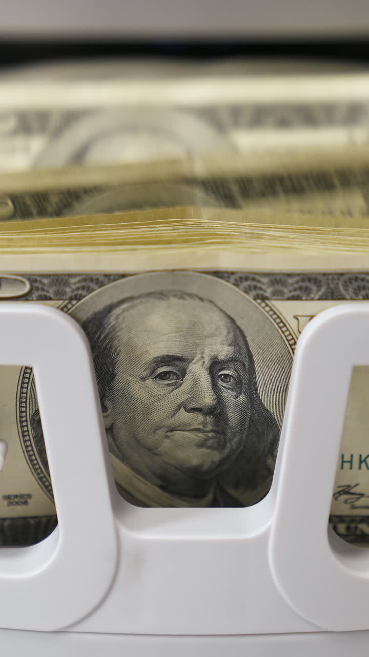 Counting process of dollar banknotes. Automated financial operations. Currency counting machine counts hundred dollar bills. Banking and commercial activity. Close-up. Vertical video