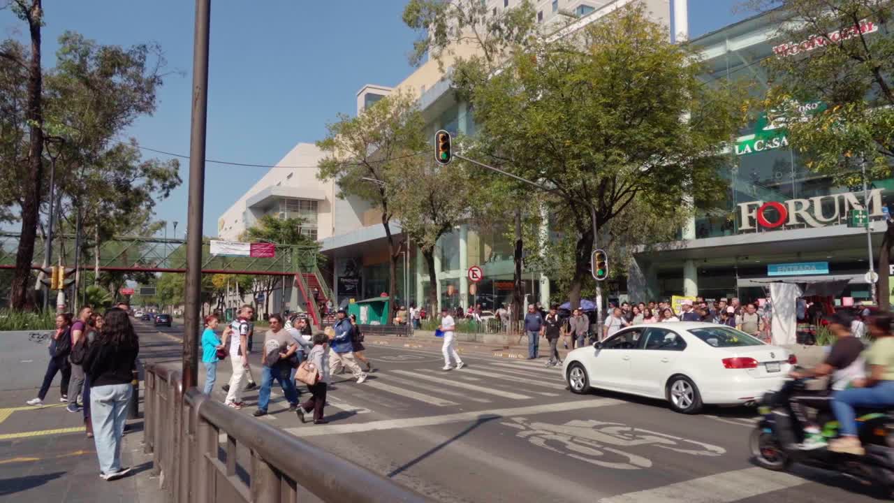 Crowd of pedestrians crossing a busy urban street near a shopping mall on a sunny day
