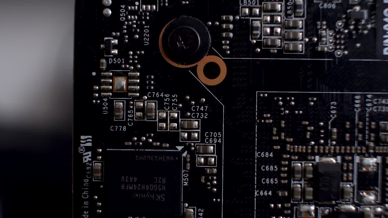 задняя сторона графической карты вблизи показывает печатную платку, гладкую платформу с множеством чипов и электронных компонентов.