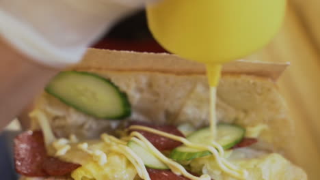 man puts mayonnaise in delicious sandwich with salami and vegetables, close shot