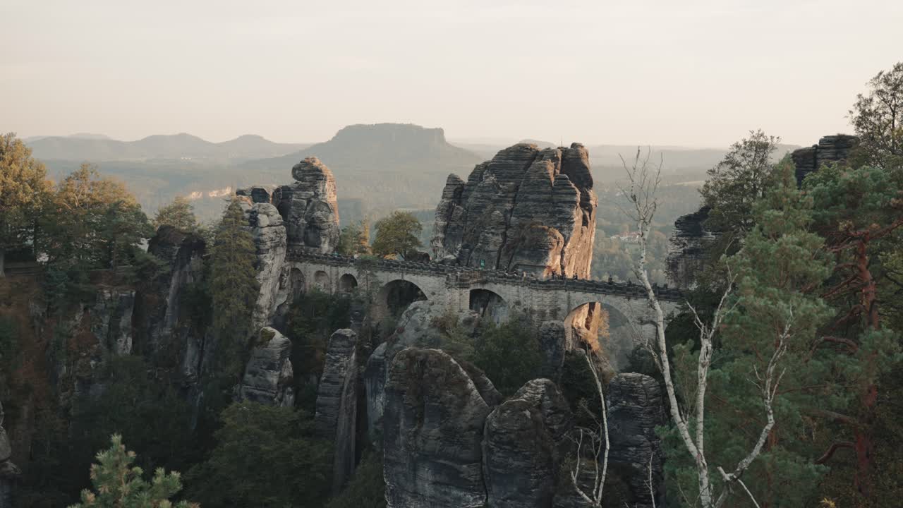amplia vista del famoso puente bastion en sajonia, alemania, cerca de dresde, construido en las rocas con su impresionante paisaje mientras la gente camina sobre él durante la puesta de sol.