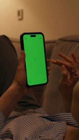 persona usando un teléfono inteligente con una pantalla verde en un sofá