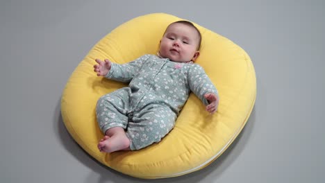 smiling baby lying on his back on a yellow comfy round cushion - high-angle shot