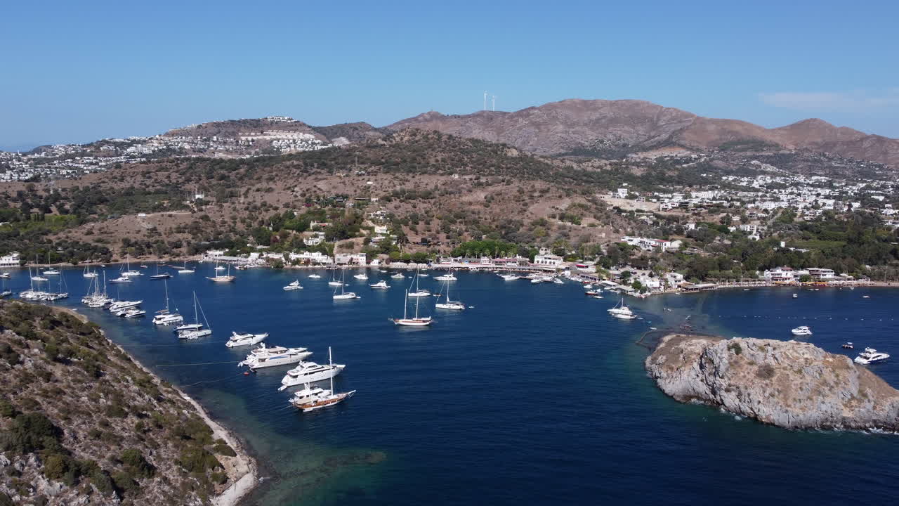 Aerial flying forward over coast of Gumusluk, boats anchored on sunny day