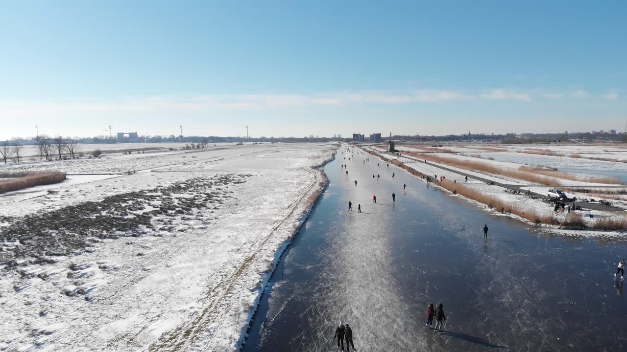 Dutch people winter ice skating on frozen canal near old windmill, aerial view