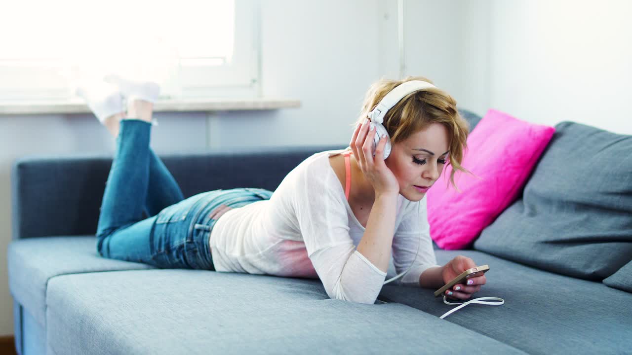 여자가 소파에 누워서 음악을 듣고 있다