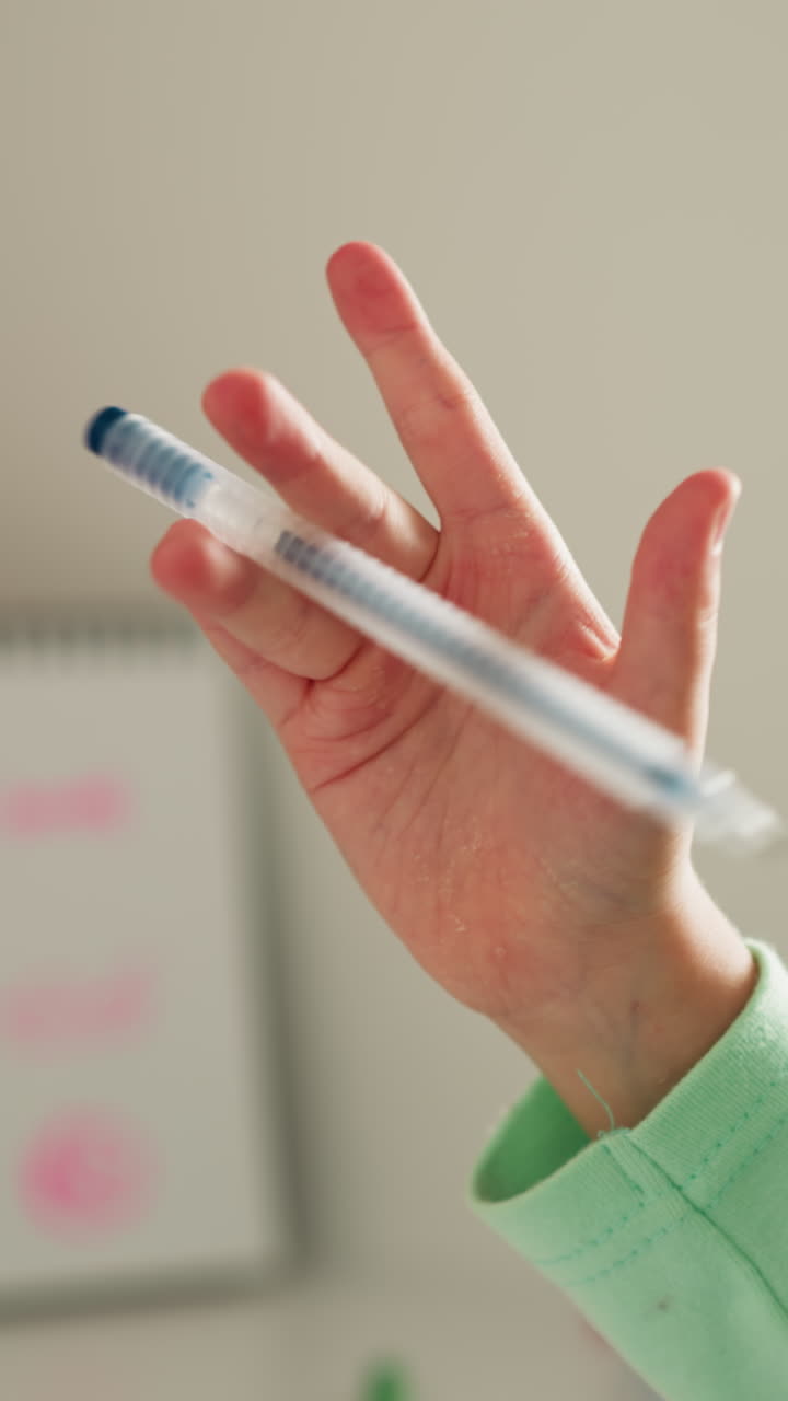 小さな女の子がクラスで指でペンを回すことを学びます 休憩のクローズアップで 疲れた手を学校のクラスでトリックで練習します 楽しいレッスンで