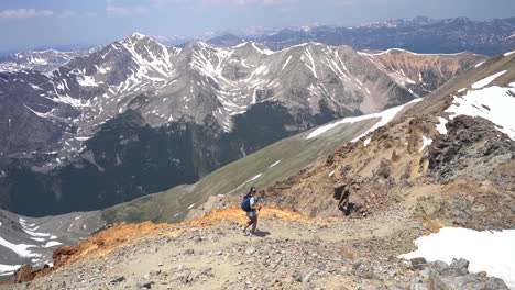 female mountaineer in vastness of rocky mountains, walking with trekking poles on top of hill