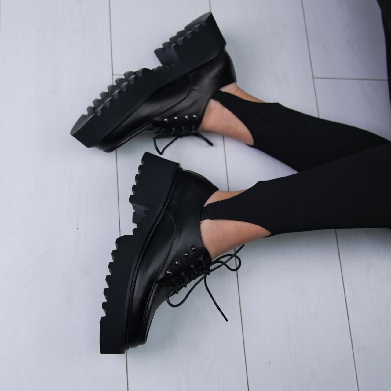 Fashionable black designer shoes demonstration. Model in black leggings sits on the floor wearing tractor-soled footwear. Top view