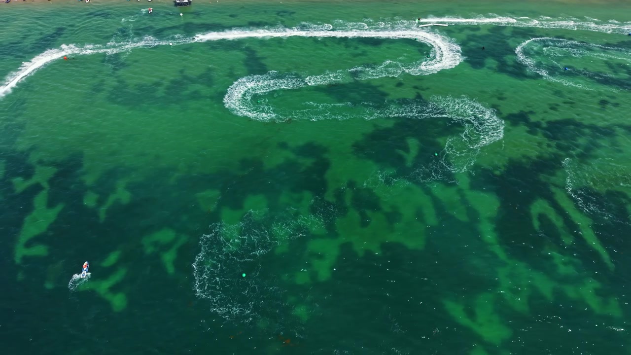 Jet ski racing takes place on clear water with multiple jet skis in action on a sunny day in a coastal area
