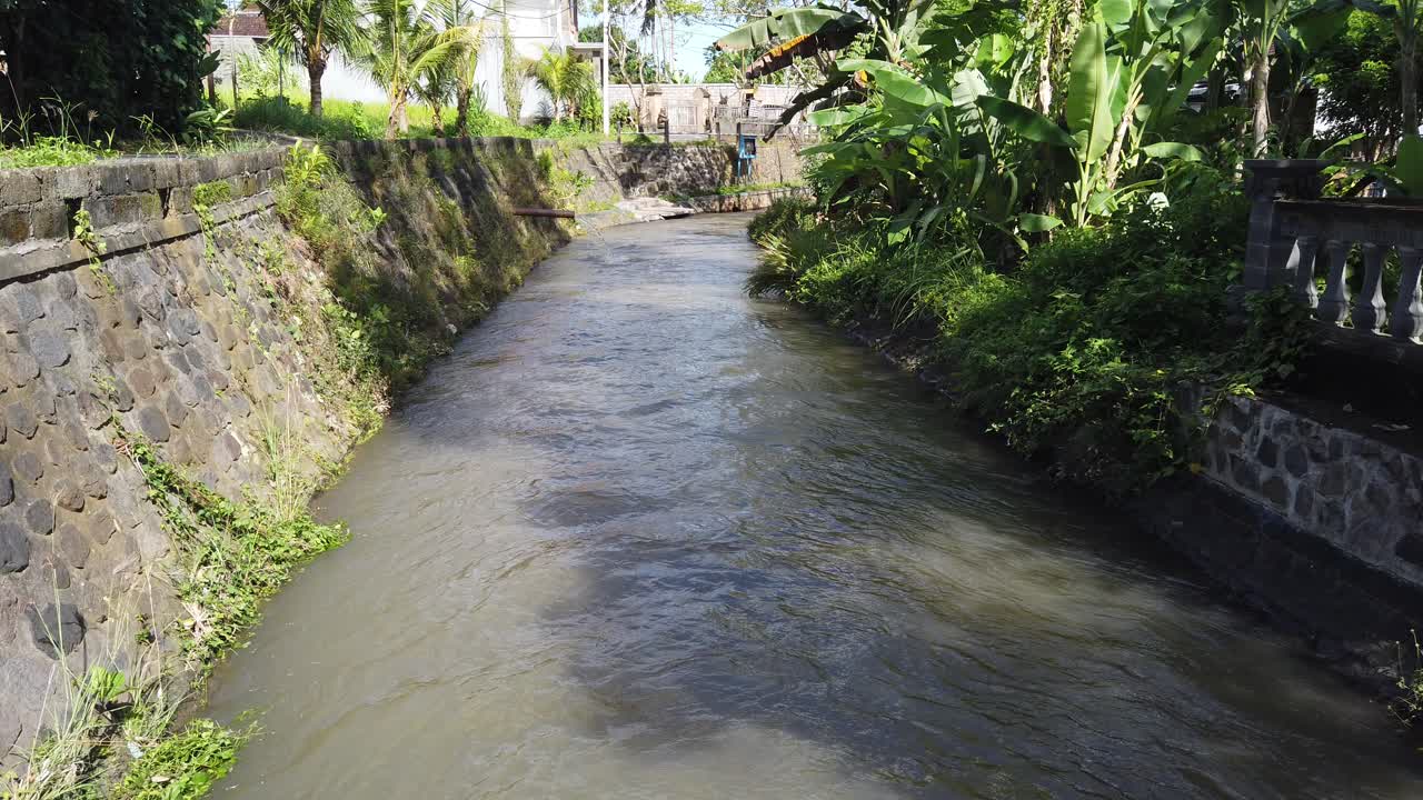 camino del río balinés sudeste de asia, canal de agua marrón gianyar bali, paisaje diurno de indonesia con árboles de plátano, viento, luz clara