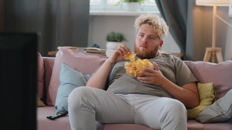 obese man eating chips and watching tv at home