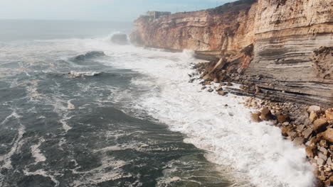 foto aérea de una playa rocosa con olas que se estrellan en nazare, portugal