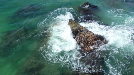disparo estático de una roca en la línea costera con las olas chocando contra ella, mar de color turquesa