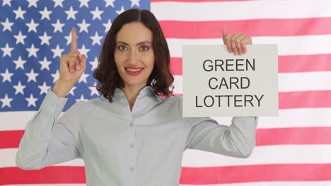 woman holding 'green card lottery' sign in front of an american flag