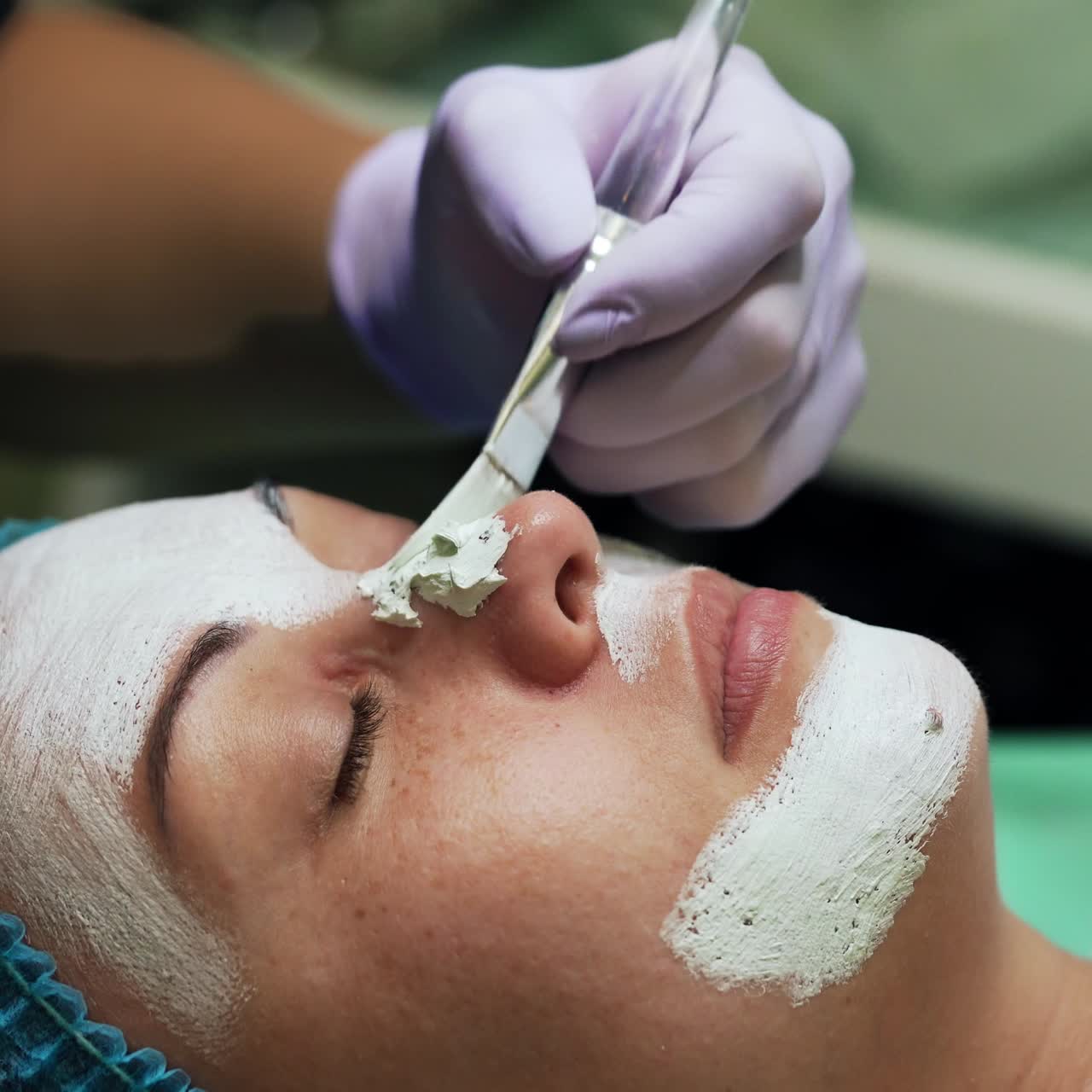 Covering Caucasian woman's face with white mask. Cosmetology procedures at beauty salon. Close up