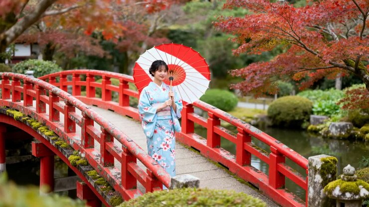 Donna in kimono in posa che sistema l'ombrellino su un ponte rosso in un giardino giapponese per uno shooting con carrellata della fotocamera