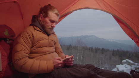 man using phone in camping tent in mountains
