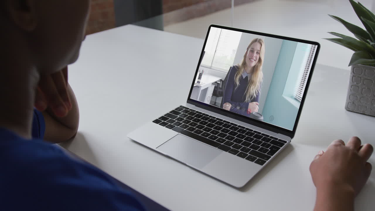 African american businesswoman sitting at desk using laptop having video call with female colleague