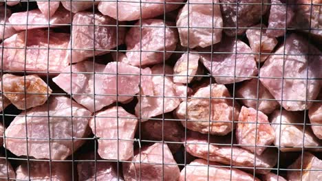 pink rose quartz rocks are packed into a wire cage and used in a gabian wall