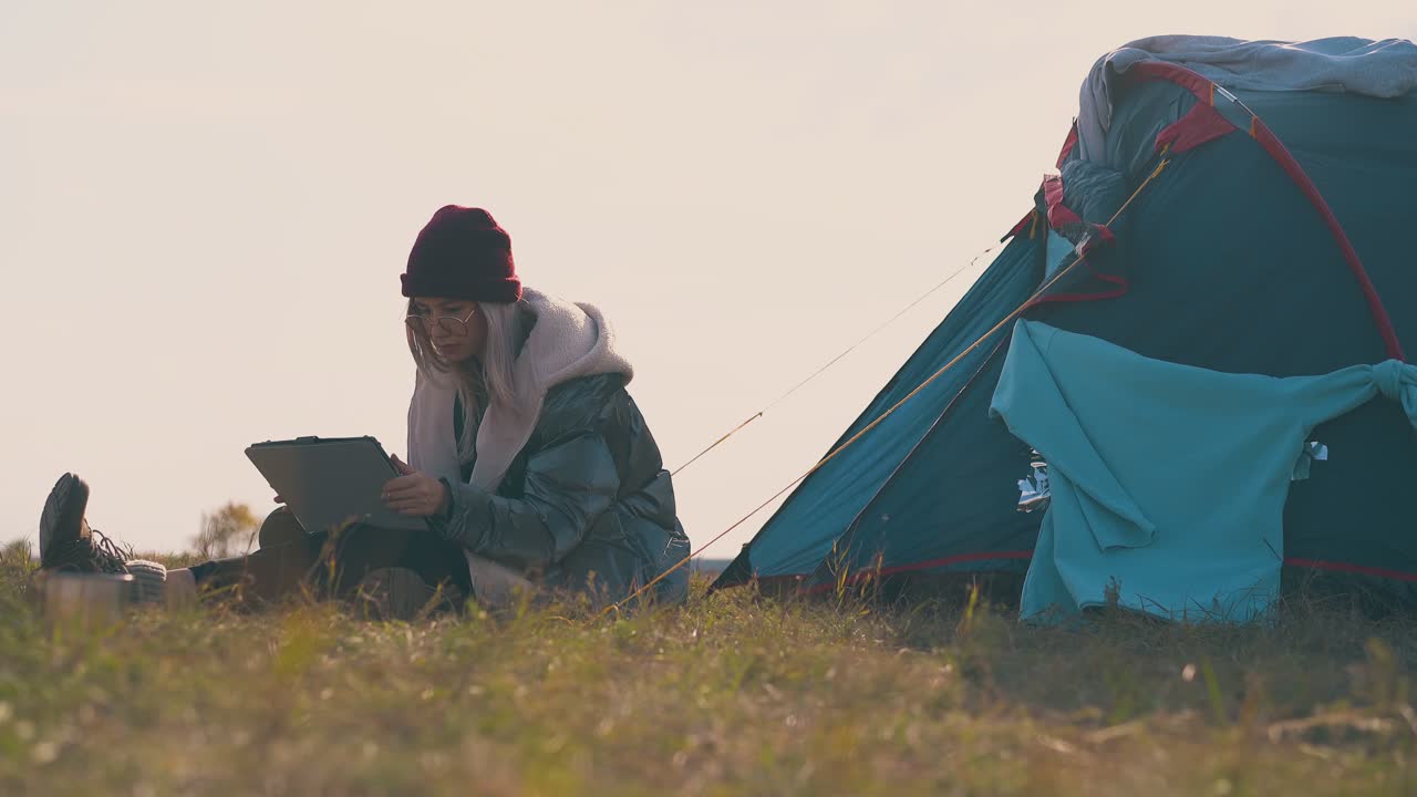 chica turista con sombrero rojo se sienta con la tableta por la tienda al atardecer
