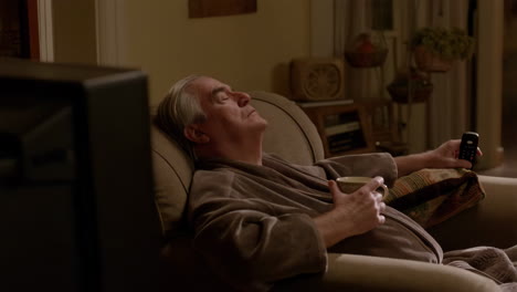 man resting in armchair with tv remote and mug