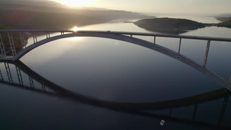 Krk-Arch-Bridge-during-sunrise-reflecting-on-water-surface,-Croatia