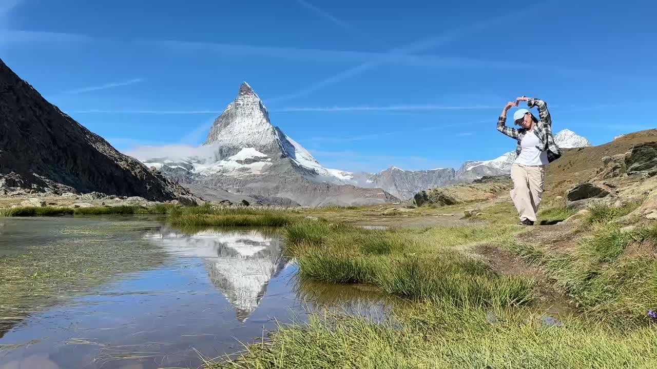 Joyful woman walking towards the camera and making a love heart gesture with her arms in front of the scenic Matterhorn peak in Switzerland