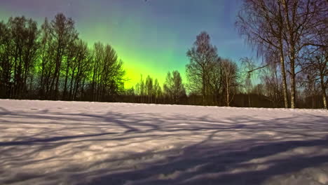 Zeitraffer-Bunter-Nordlichter,-Die-Nachts-über-Einem-Schneebedeckten-Feld-Mit-Wald-Im-Hintergrund-Tanzen