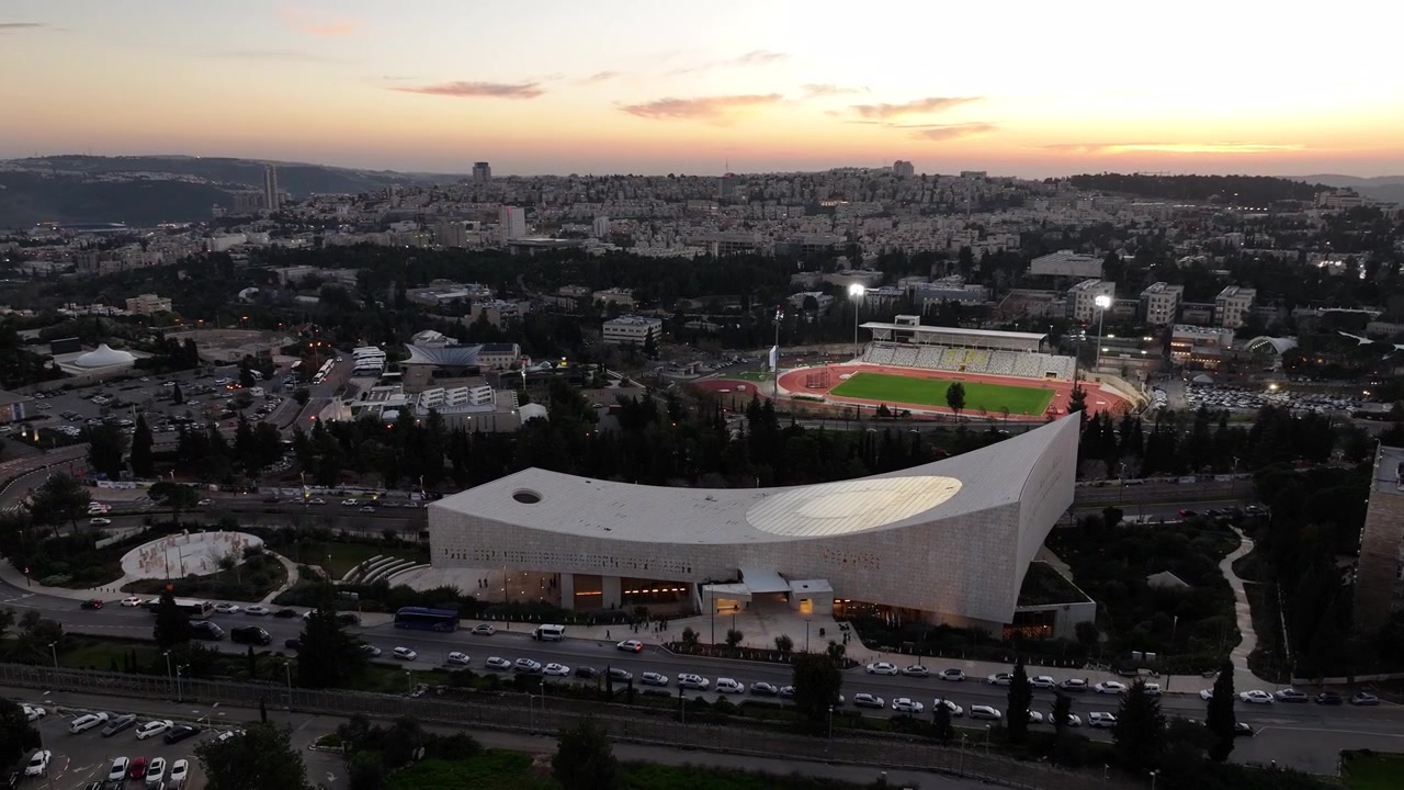 Solnedgangsutsikt over den moderne bygningen til Israels nasjonalbibliotek og opplyst sportsstadion i Givat Ram, Jerusalem.