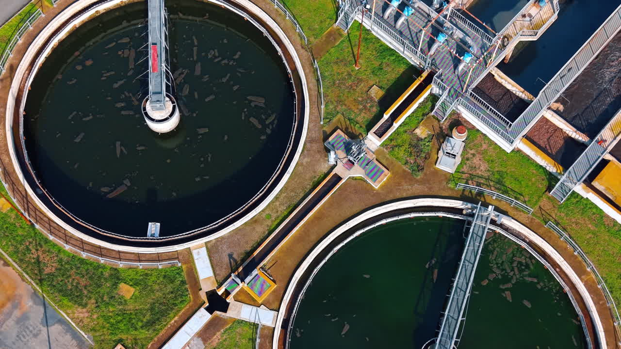 Top down view of wastewater clarifier with green water. Circular sedimentation tank filled with green water and a rotating bridge