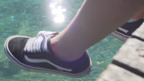 girl dangling feet over jetty above crystal clear lagoon water in new zealand