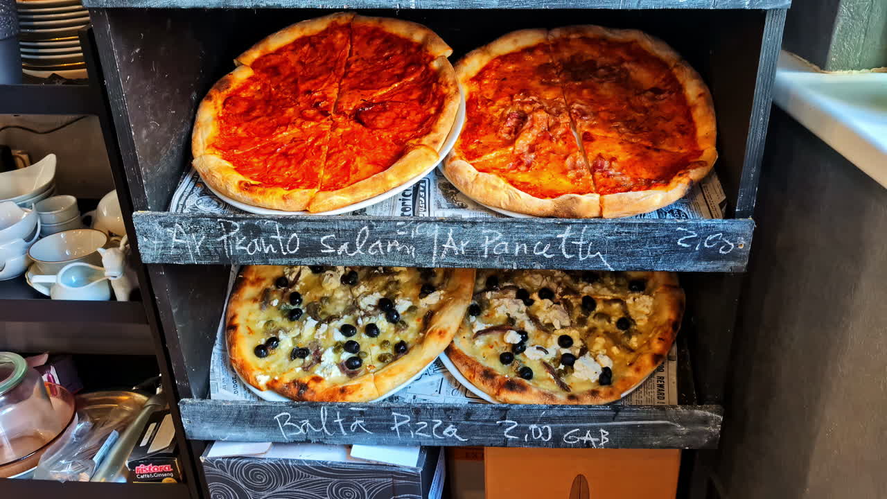 Assortment of different pizzas with salami and cheese displayed on a rustic wooden shelf in a Cesis, Latvia cafe